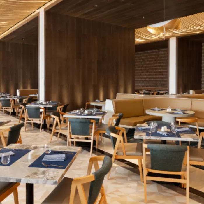 Contemporary restaurant with soft lighting, wood accents, round booths, and marble tables set for a fine dining experience.