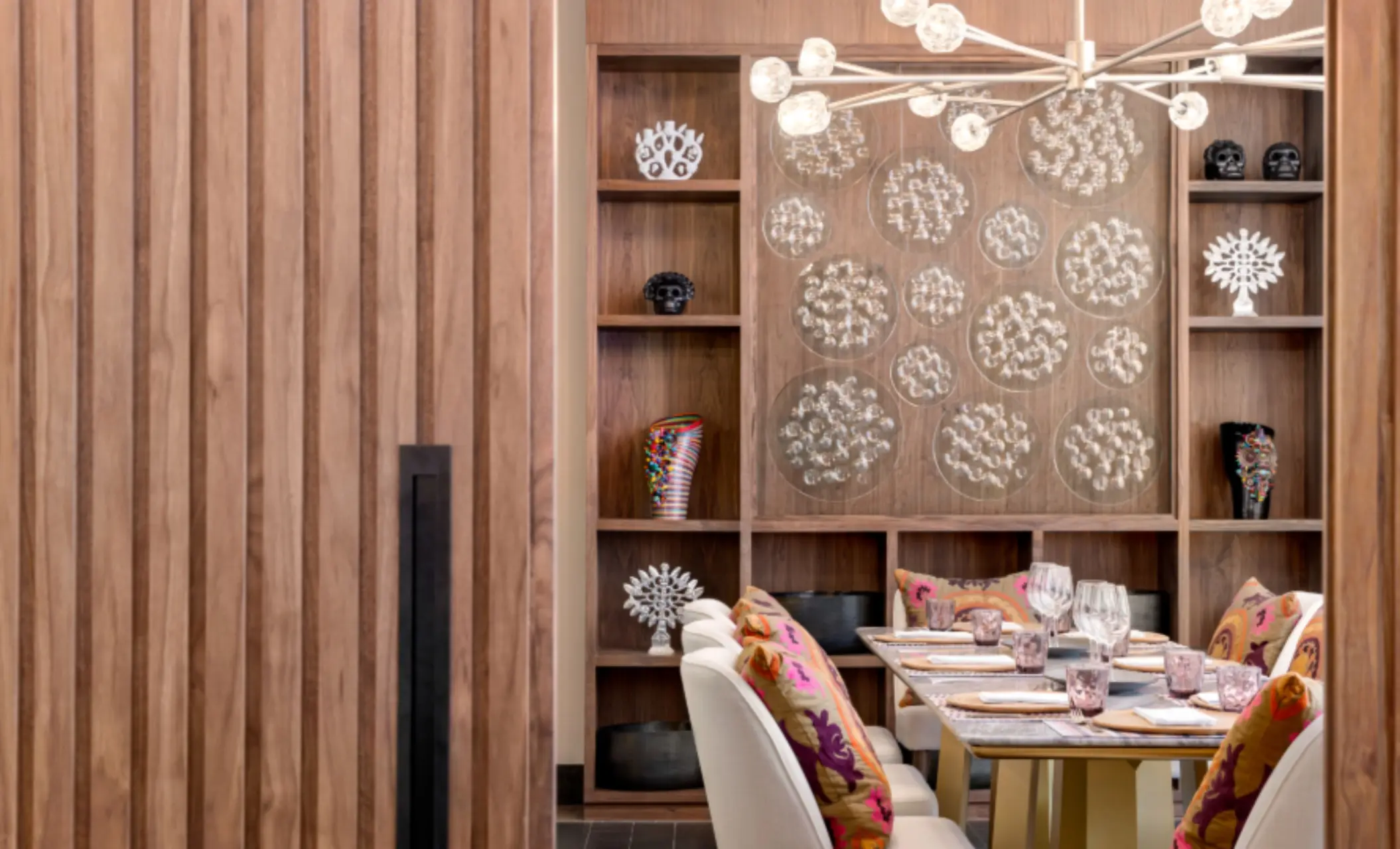 Private dining room with bold Mexican decor, colorful pillows, sculptural lighting, and custom wood shelving details.