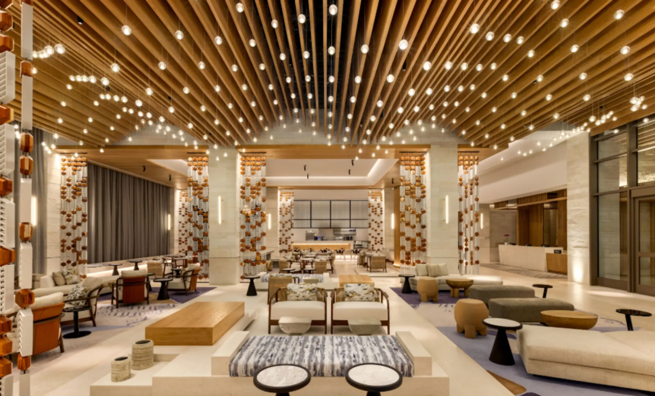 Spacious lobby with wood ceiling slats, pendant lighting, and stylish lounge seating at a luxury beachfront resort.