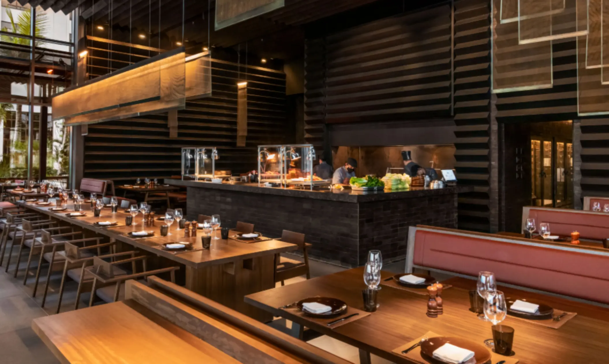 Upscale restaurant with open kitchen, wood paneling, warm lighting, and neatly arranged tables with modern place settings.