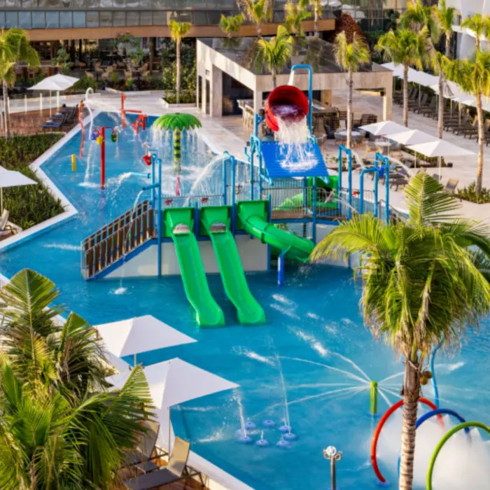 Colorful kids’ splash park with waterslides, spray features, and lounge chairs lining the pool at a family-friendly resort.