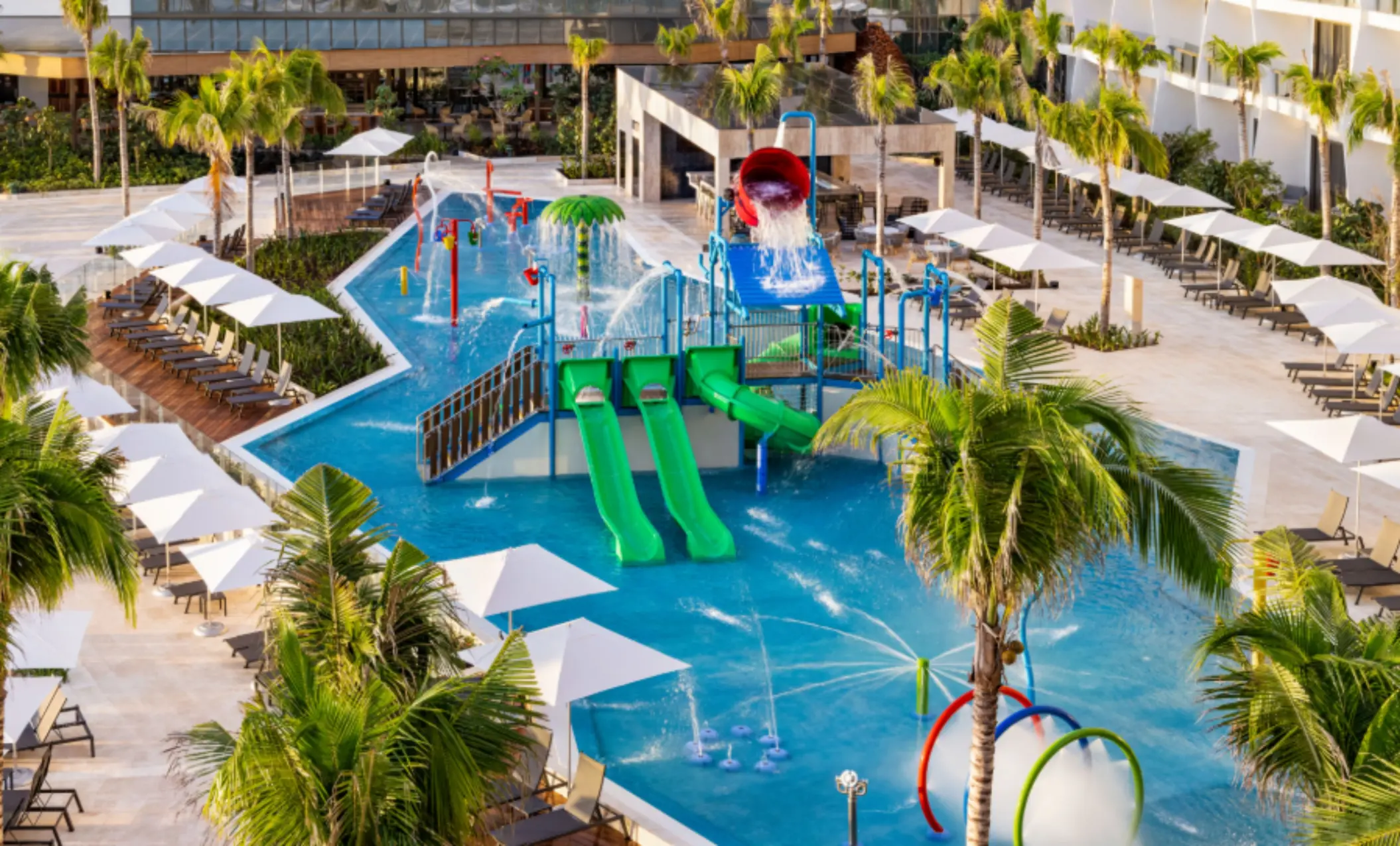 Colorful kids’ splash park with waterslides, spray features, and lounge chairs lining the pool at a family-friendly resort.