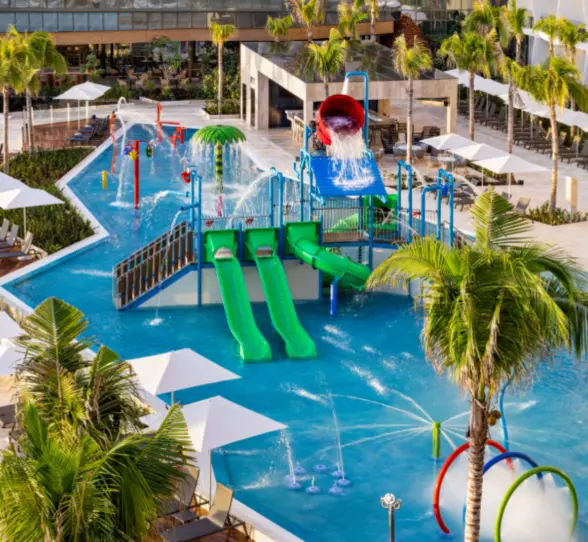 Colorful kids’ splash park with waterslides, spray features, and lounge chairs lining the pool at a family-friendly resort.