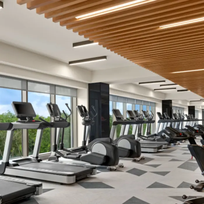 Spacious fitness center with treadmills, stationary bikes, and large windows overlooking tropical greenery and blue skies.