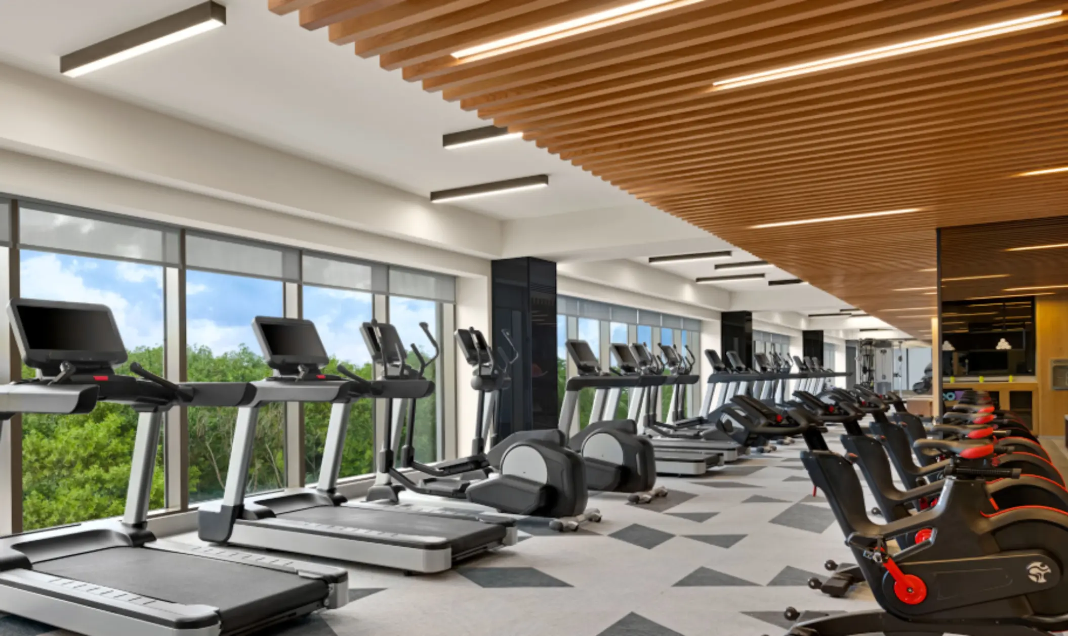 Spacious fitness center with treadmills, stationary bikes, and large windows overlooking tropical greenery and blue skies.