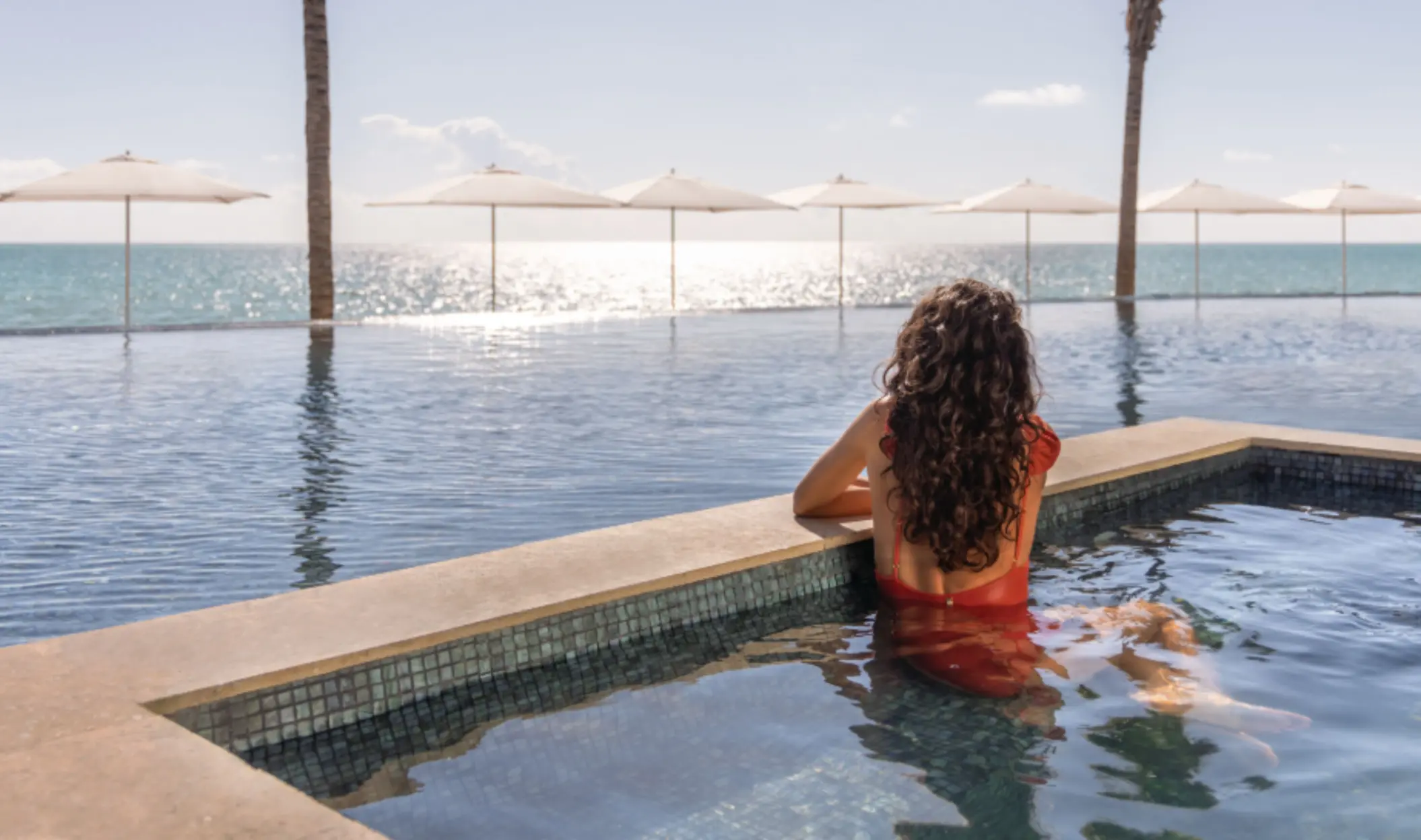 Relaxing beachfront infinity pool with white umbrellas and ocean horizon in the background.