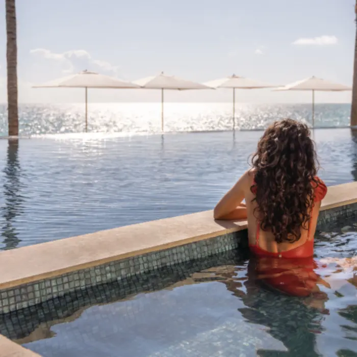 Relaxing beachfront infinity pool with white umbrellas and ocean horizon in the background.