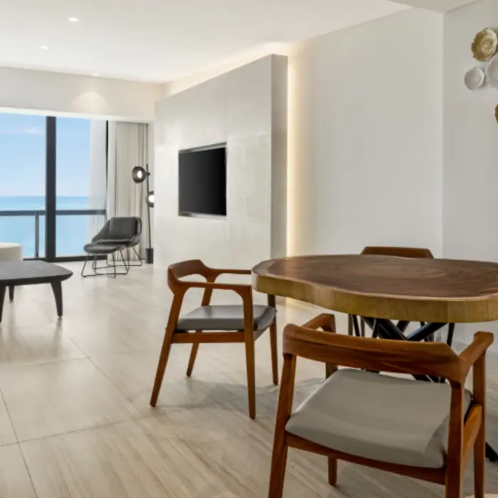 Oceanview suite living area with modern furnishings, wooden dining table, and large windows facing the sea.