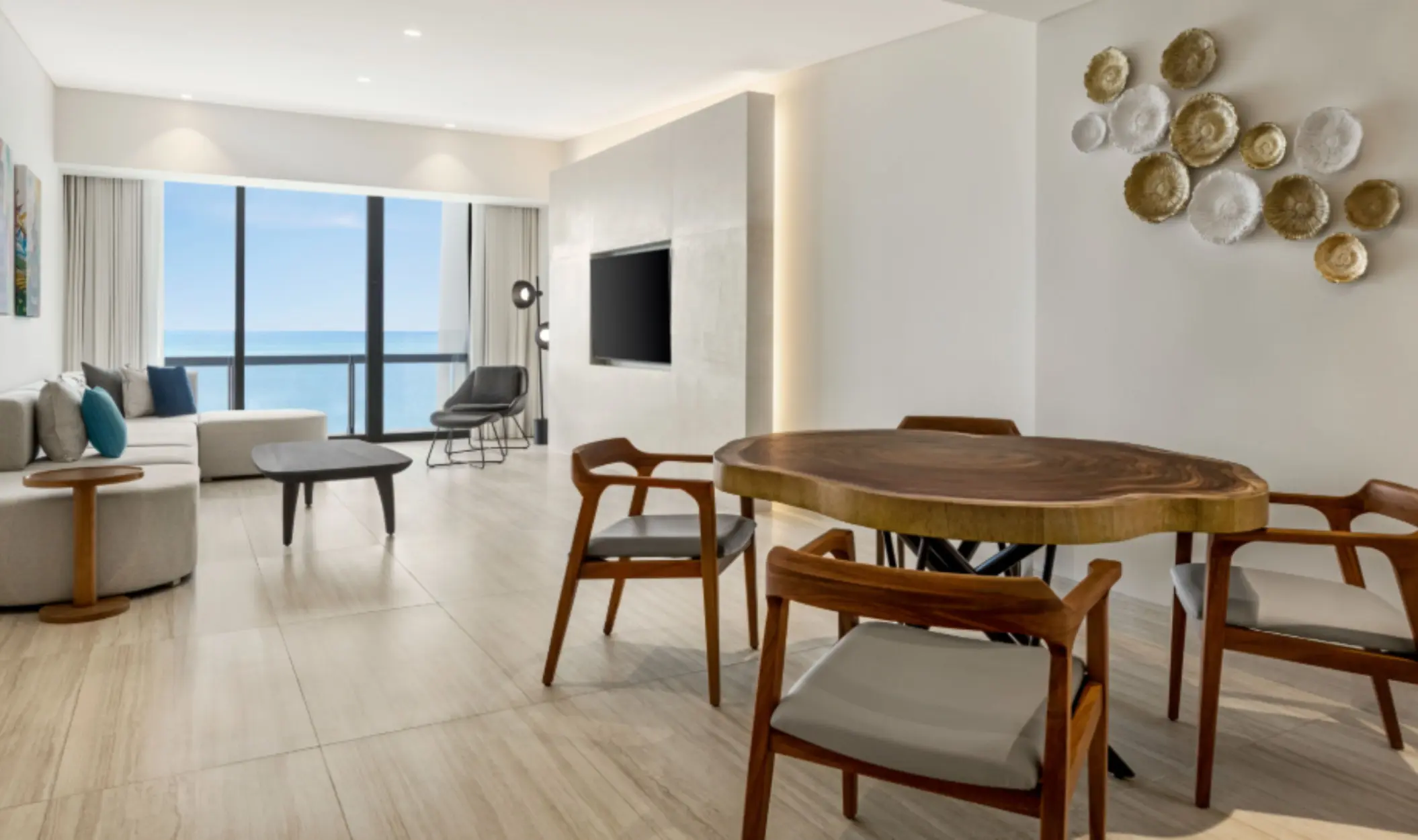Oceanview suite living area with modern furnishings, wooden dining table, and large windows facing the sea.