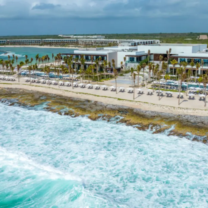 Aerial view of modern beachfront resort with loungers and palm trees along the rocky Caribbean shoreline
