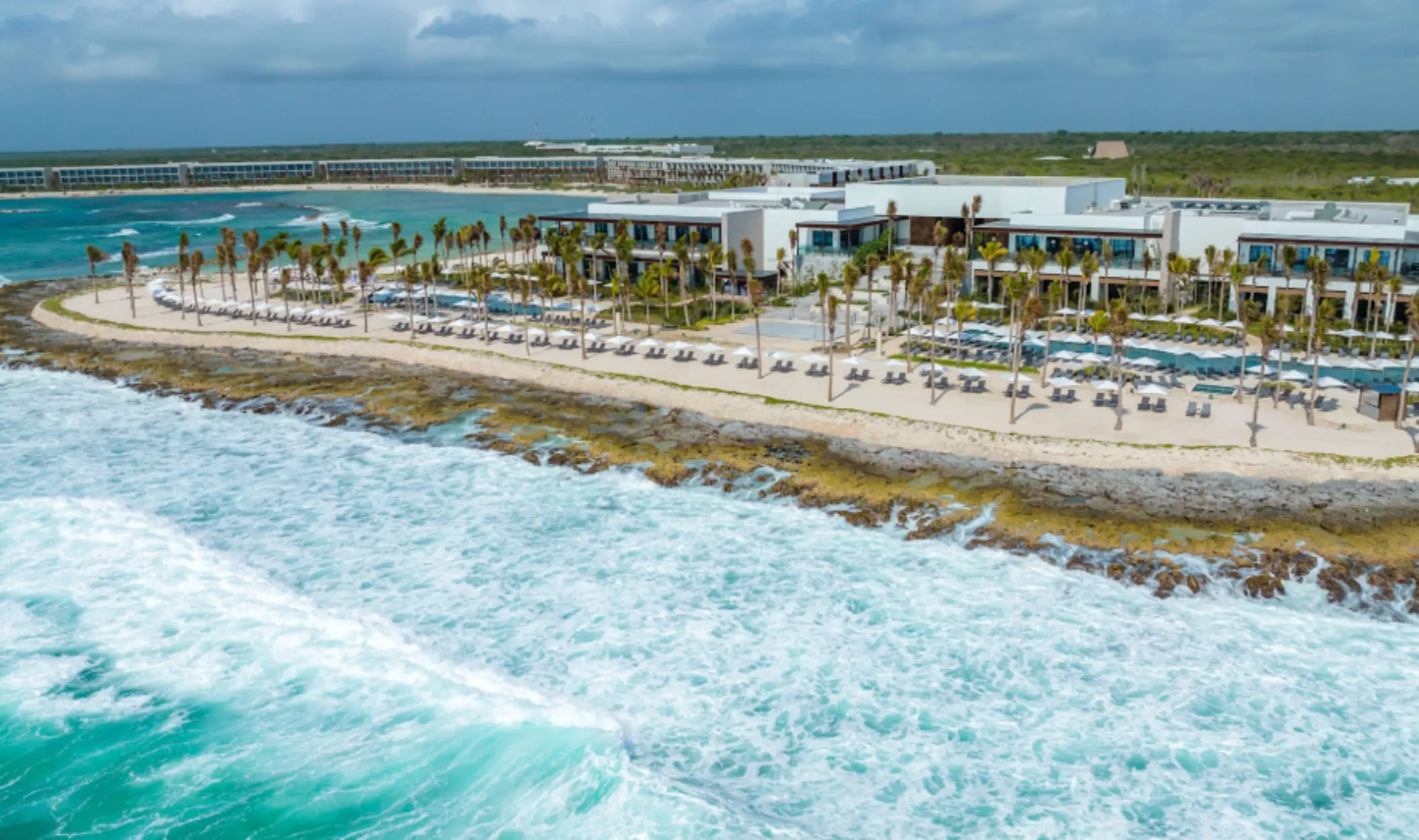 Aerial view of modern beachfront resort with loungers and palm trees along the rocky Caribbean shoreline