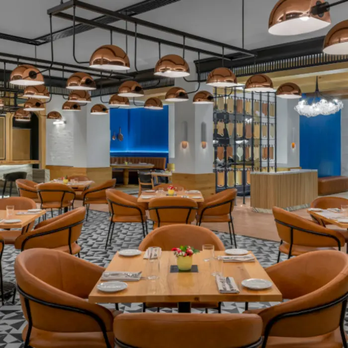 Trendy indoor restaurant with leather chairs, geometric tile flooring, and open kitchen with pizza oven.