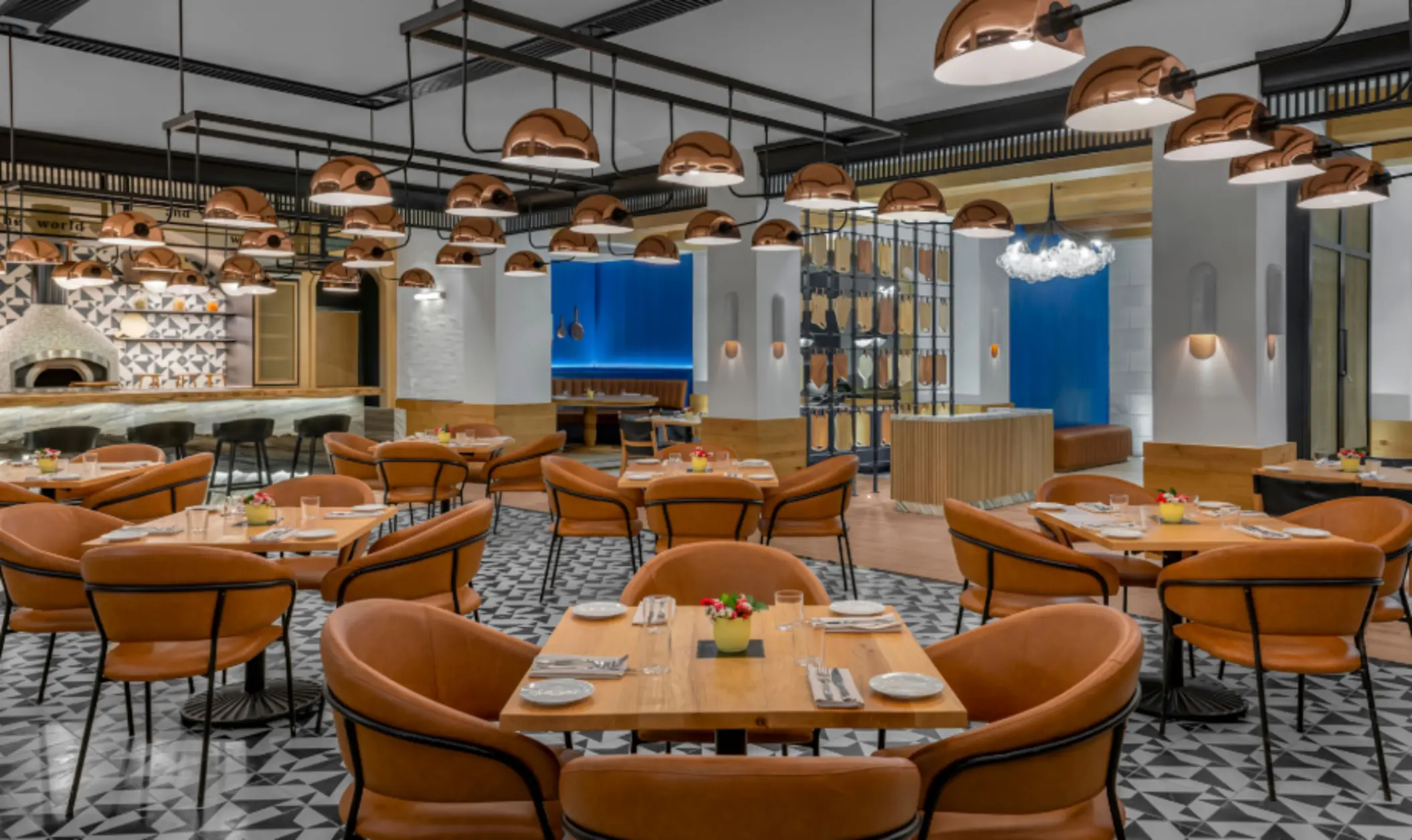 Trendy indoor restaurant with leather chairs, geometric tile flooring, and open kitchen with pizza oven.