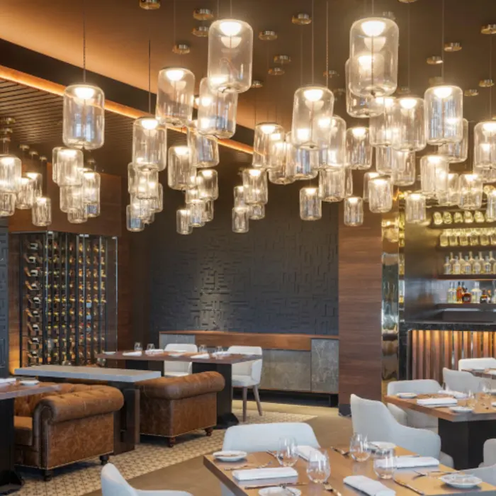 Elegant restaurant with warm lighting, wine cellar wall, tan leather seating, and hanging glass lamps.