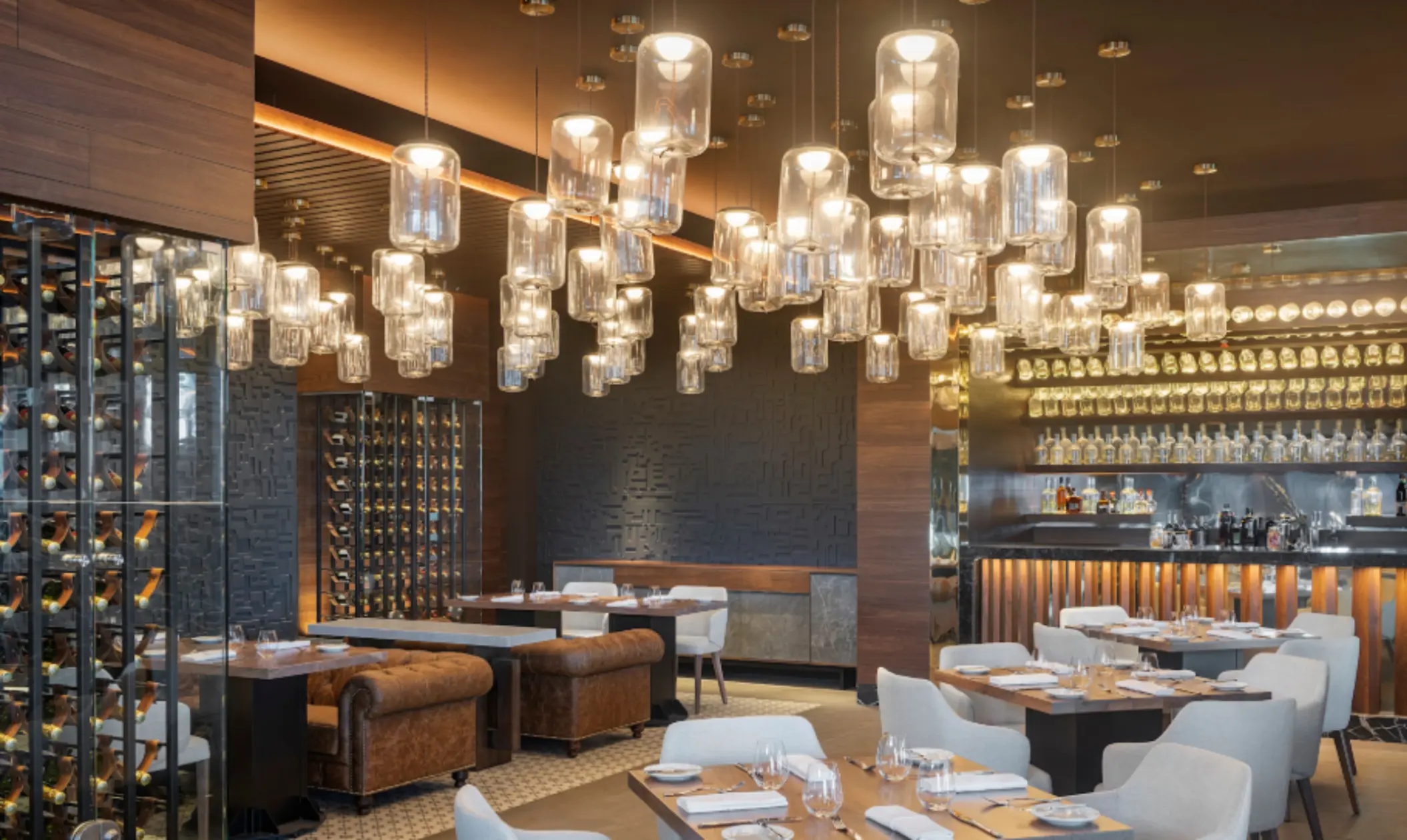 Elegant restaurant with warm lighting, wine cellar wall, tan leather seating, and hanging glass lamps.