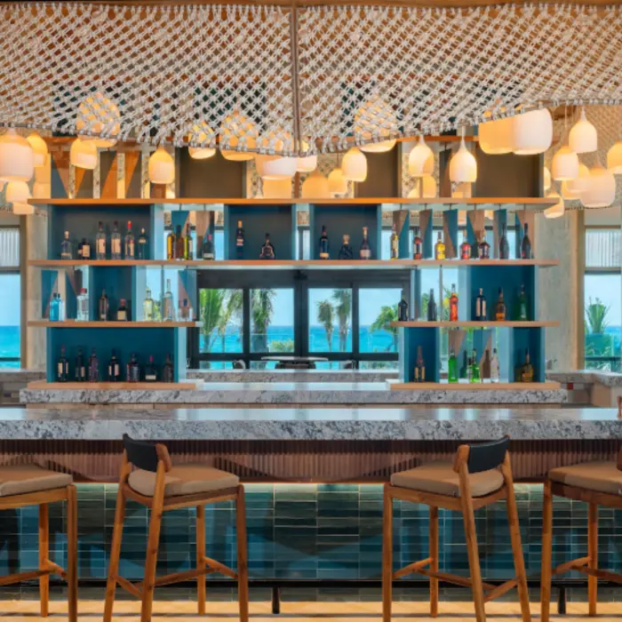 Stylish beachfront bar with ocean views, sleek shelving, marble countertops, and modern hanging lights.