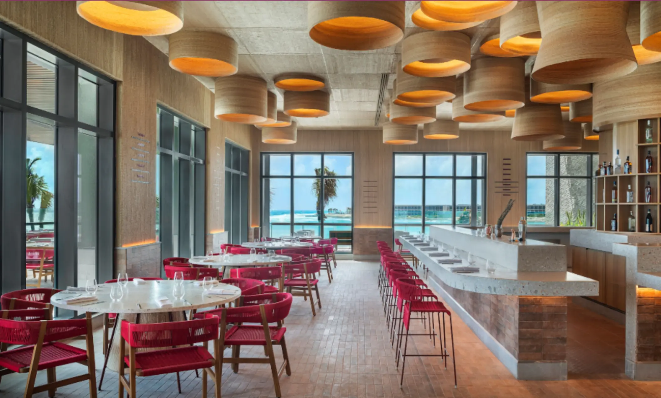 Chic beachfront dining space with ocean views, bold lighting, and red-accented seating in a stylish layout.