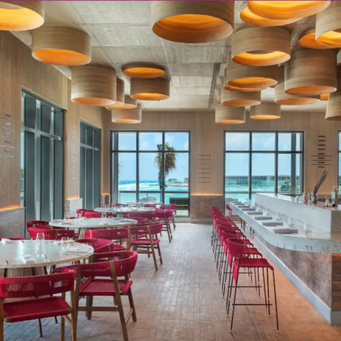 Chic beachfront dining space with ocean views, bold lighting, and red-accented seating in a stylish layout.