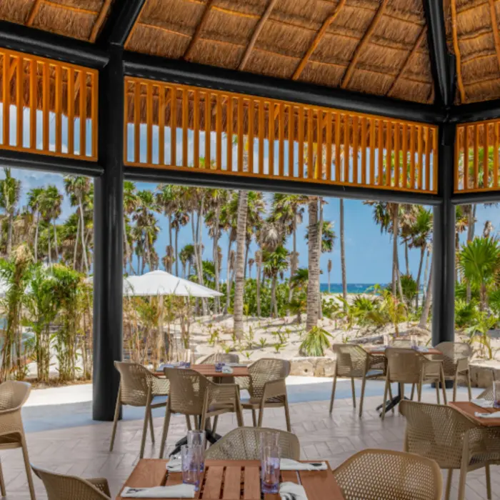 Outdoor thatched-roof dining area with views of palm trees, sandy pathways, and lush tropical greenery.