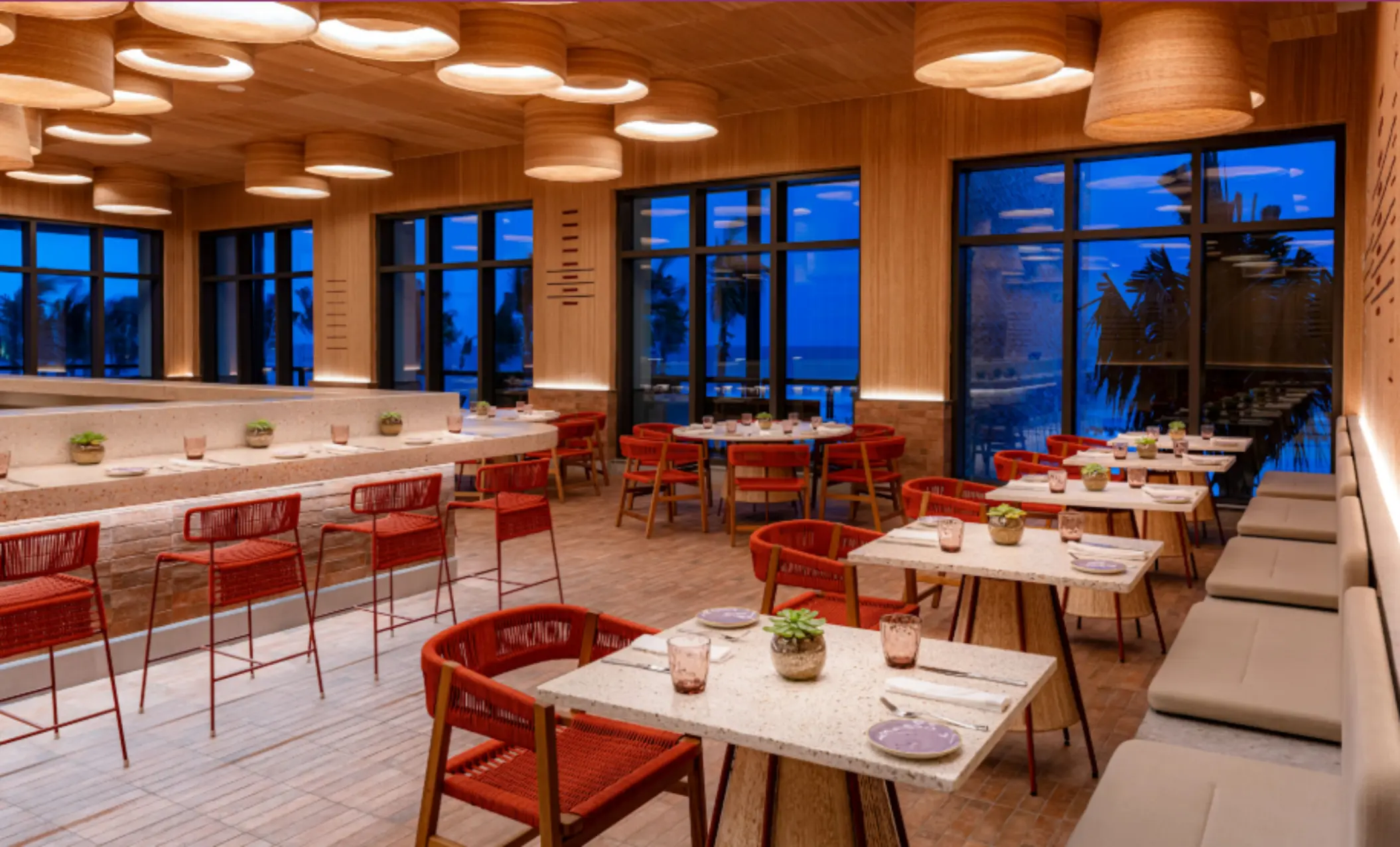 Modern dining room with natural wood accents, ocean views, and warm lighting that creates a cozy ambiance.