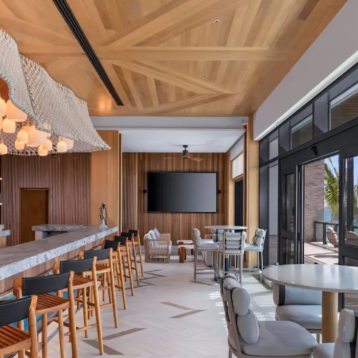 Stylish indoor lounge bar with marble countertop, wood ceiling, hanging lights, and ocean-view seating area.