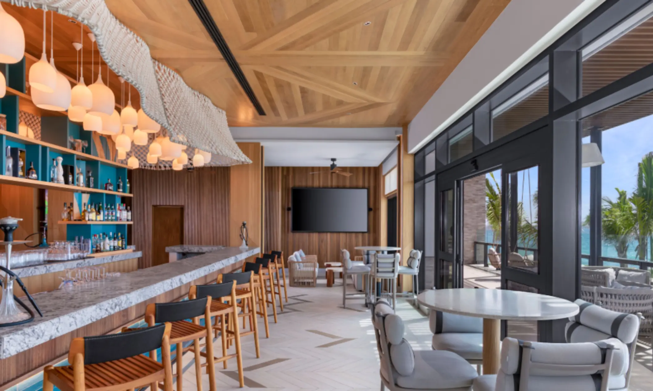 Stylish indoor lounge bar with marble countertop, wood ceiling, hanging lights, and ocean-view seating area.