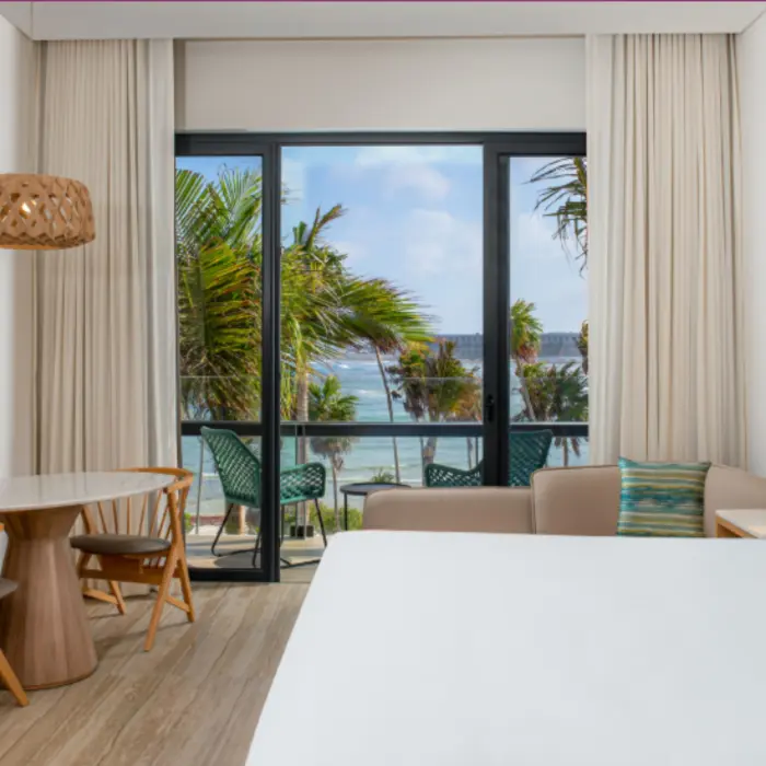 Room with king bed, palm tree and ocean views, natural wood accents, and private balcony seating.