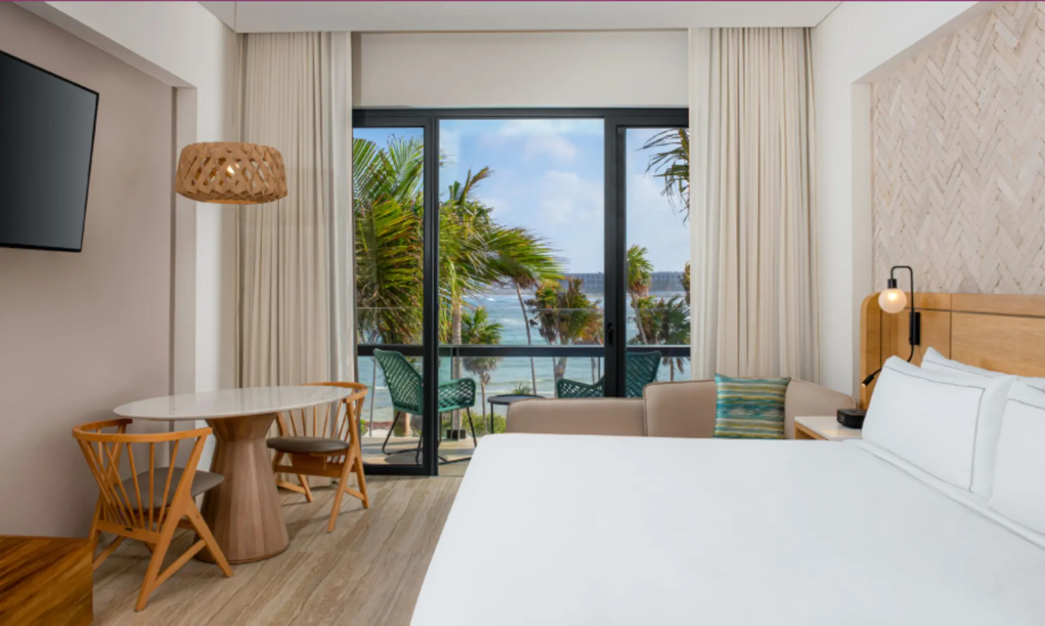 Room with king bed, palm tree and ocean views, natural wood accents, and private balcony seating.