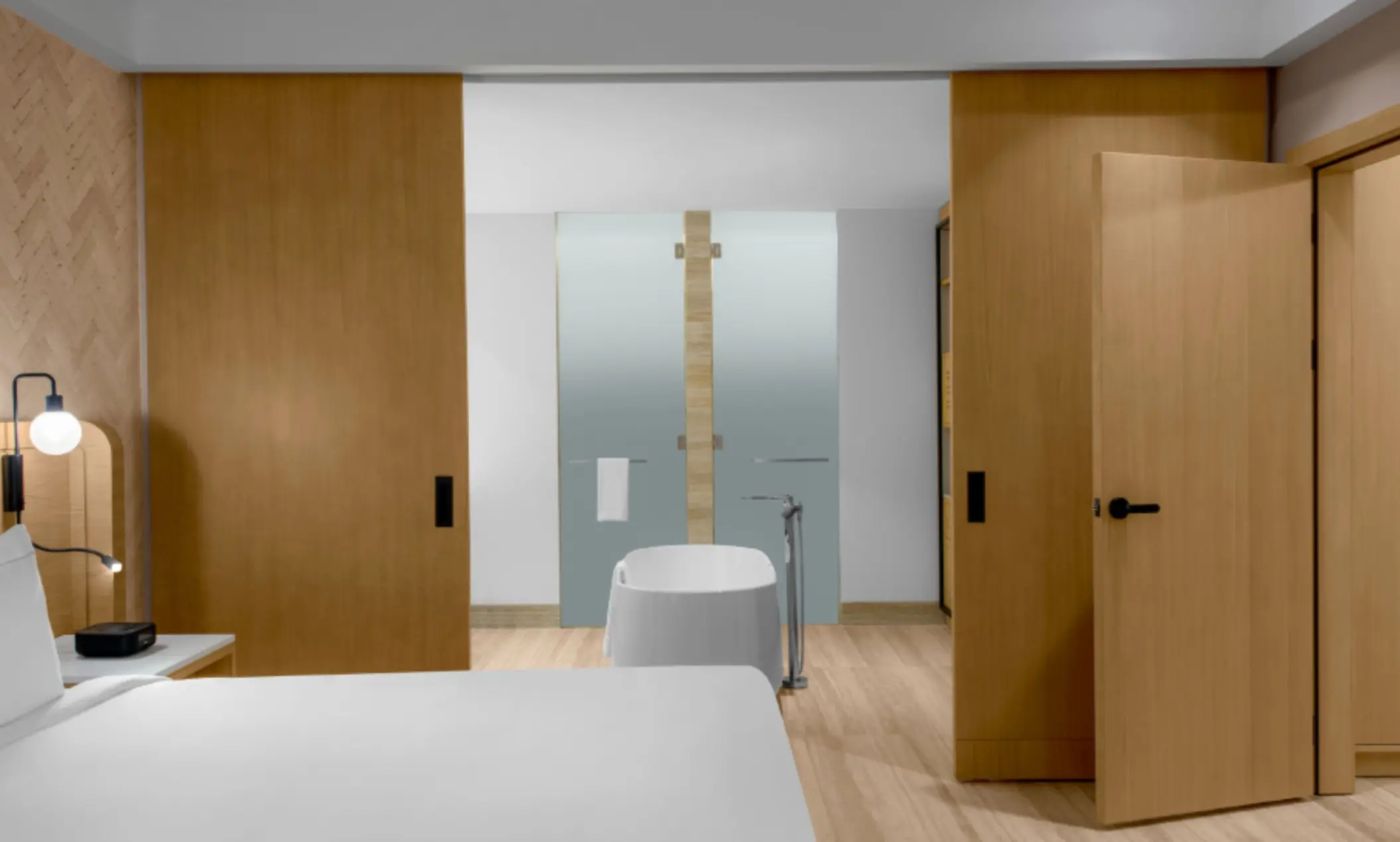 Suite interior with sliding doors revealing a freestanding bathtub and minimalist wood bathroom design.
