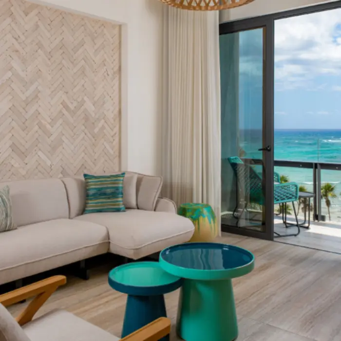 Oceanview suite with stylish beige couch, vibrant accent tables, and private balcony overlooking the sea.
