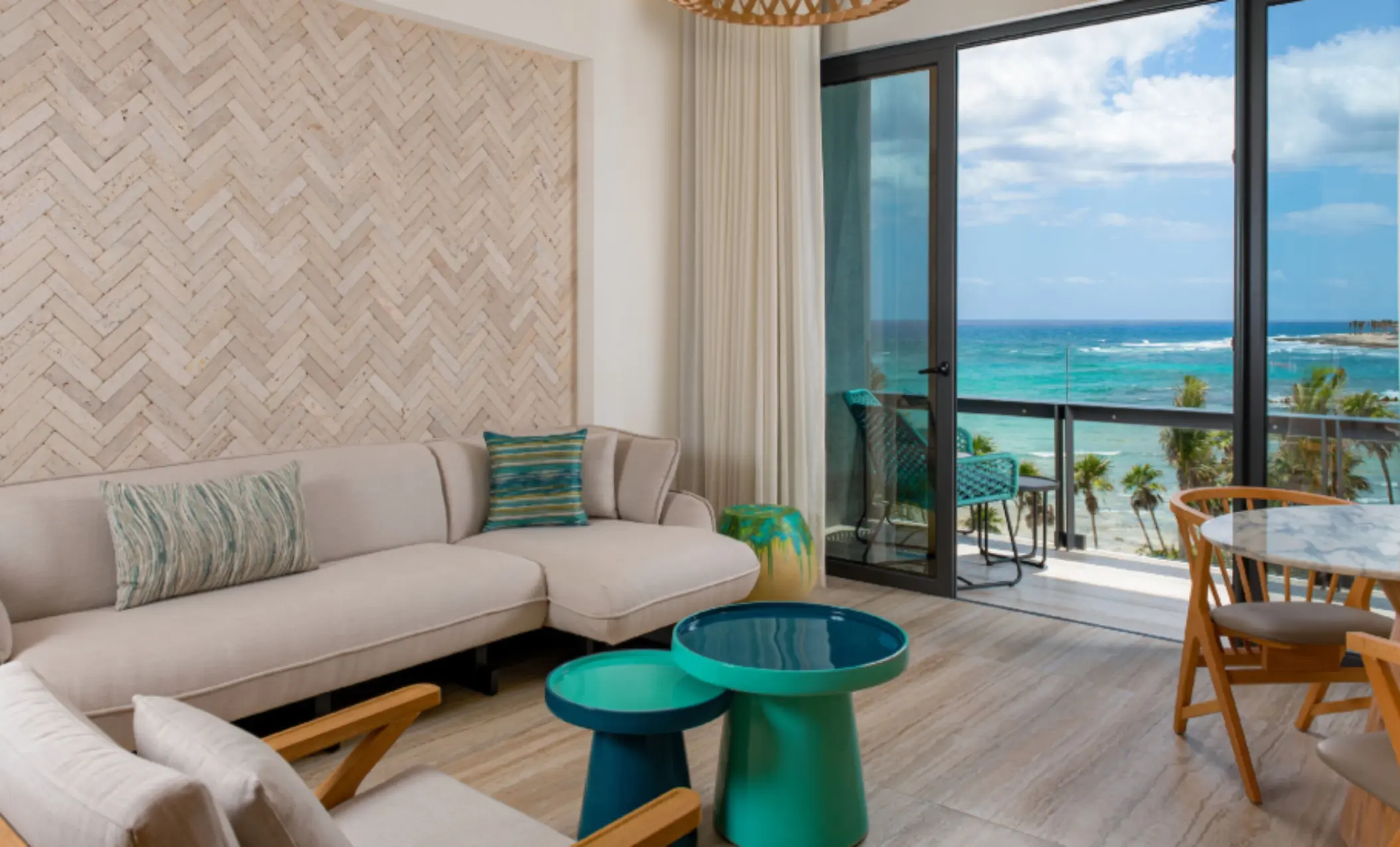 Oceanview suite with stylish beige couch, vibrant accent tables, and private balcony overlooking the sea.