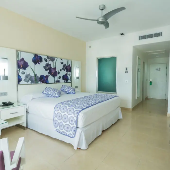 modern junior suite with a large bed, decorative headboard, white and blue bedding, and a ceiling fan.