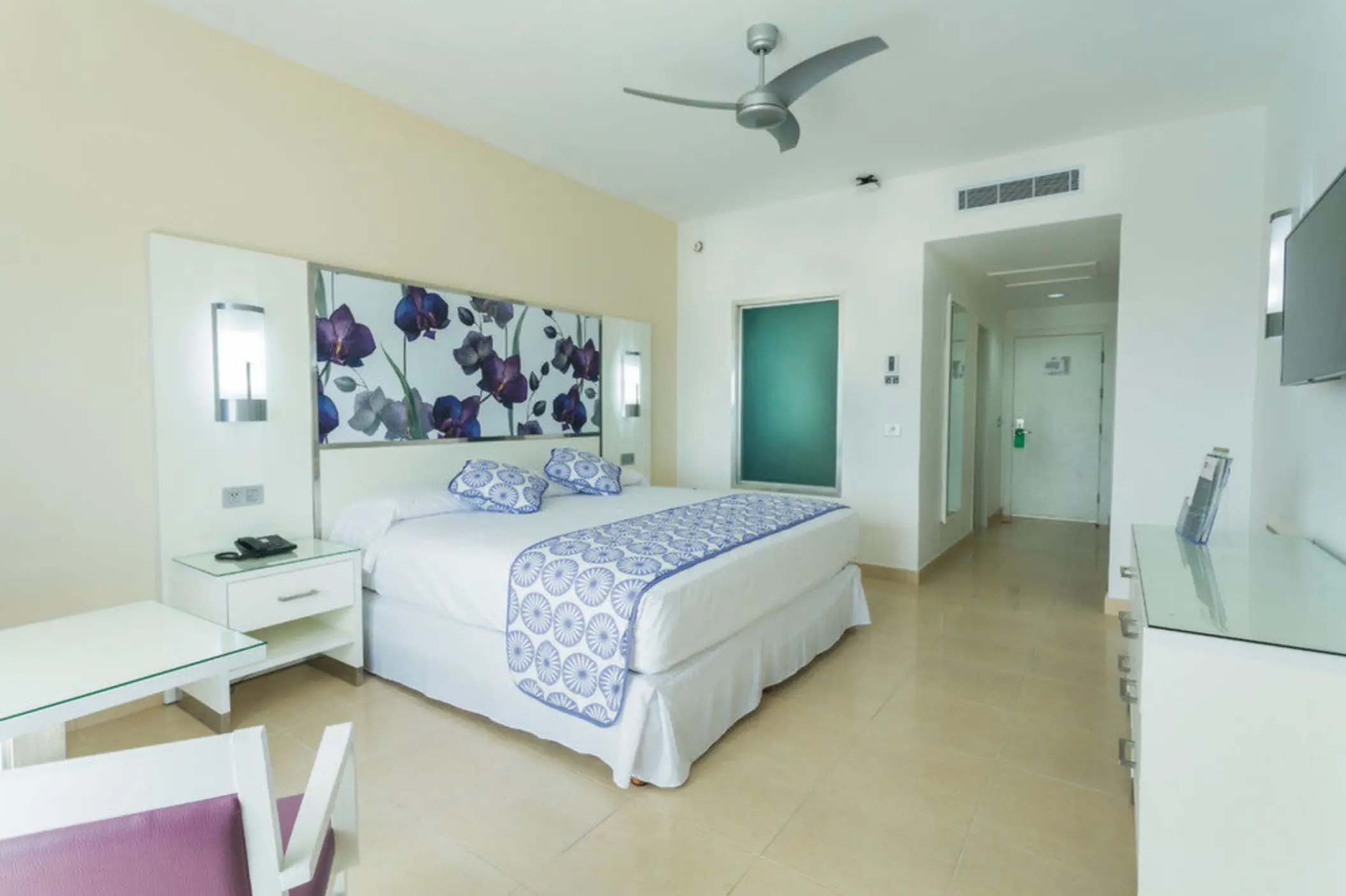 modern junior suite with a large bed, decorative headboard, white and blue bedding, and a ceiling fan.