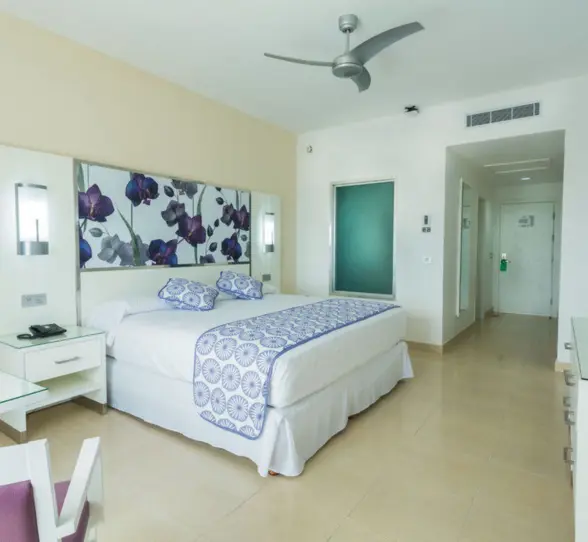 modern junior suite with a large bed, decorative headboard, white and blue bedding, and a ceiling fan.