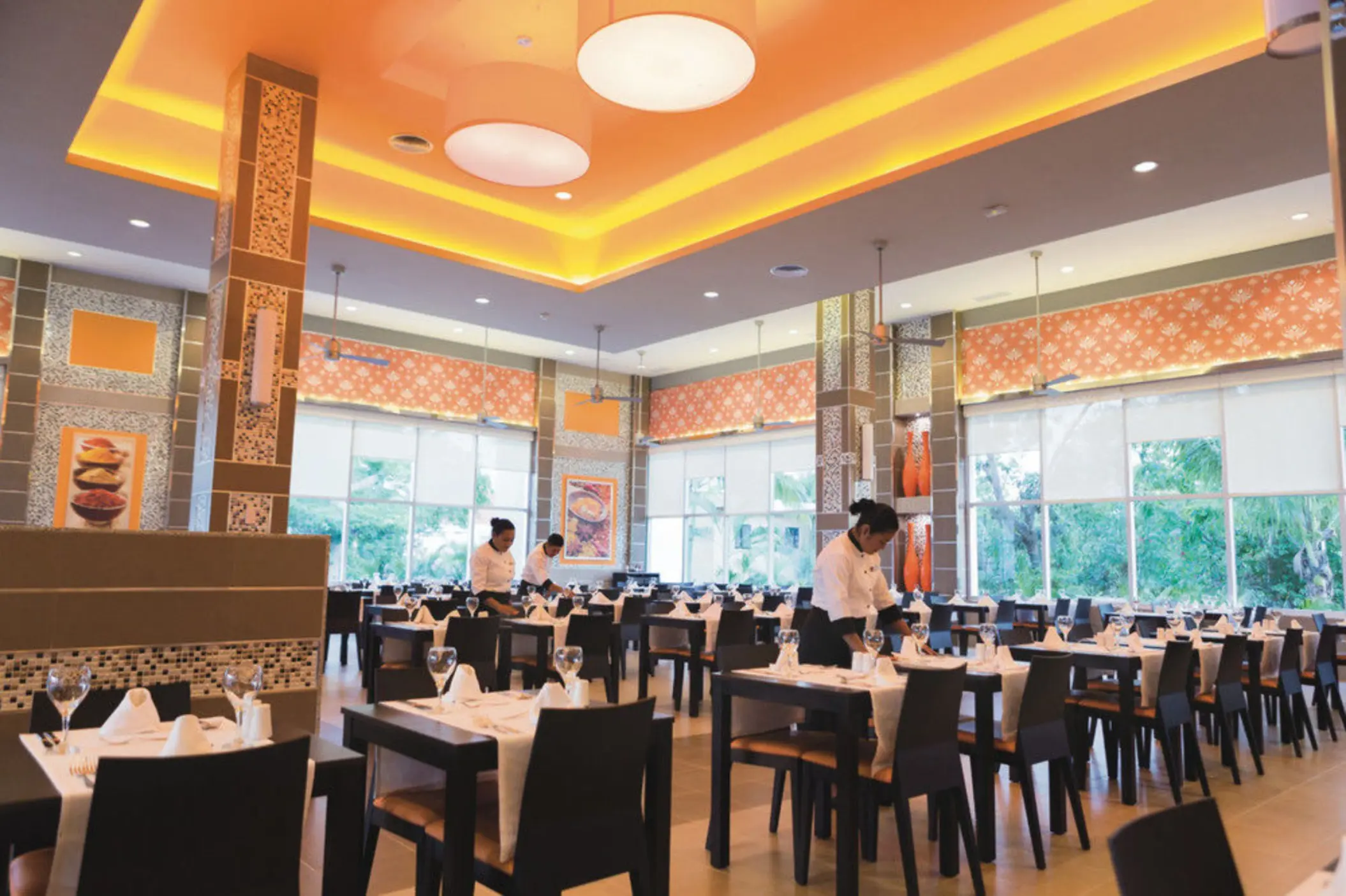 bright and elegant restaurant with neatly set tables, staff preparing for service, and large windows offering outdoor views.