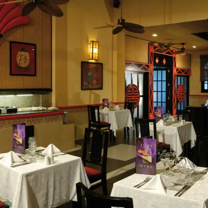 Asian-themed restaurant with red and black decor, traditional art, a buffet counter, and tables set with white tablecloths.