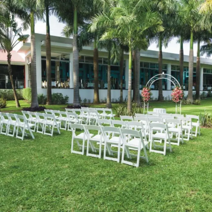 A serene outdoor garden ceremony setup on a lush green lawn, featuring rows of white folding chairs and a decorative arch.
