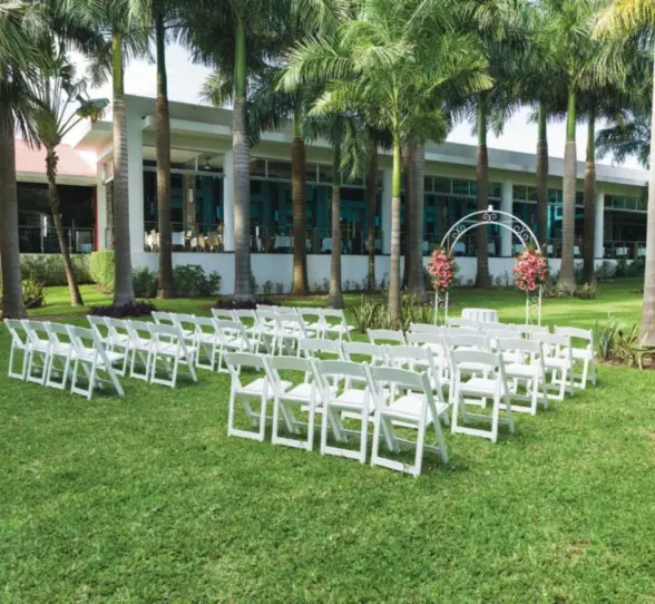 A serene outdoor garden ceremony setup on a lush green lawn, featuring rows of white folding chairs and a decorative arch.