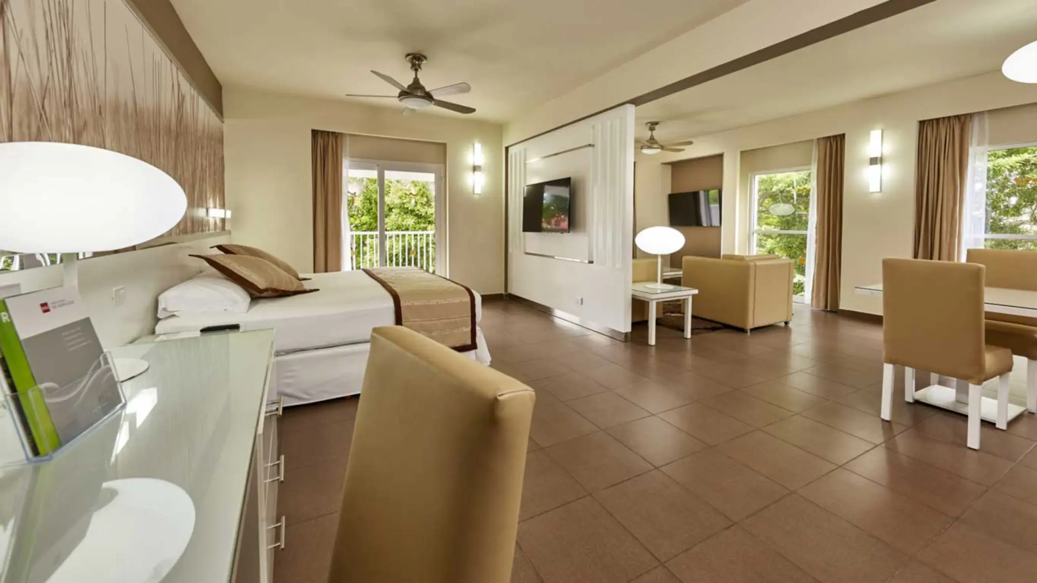 A spacious and elegantly furnished suite featuring a comfortable bed, a separate living area with a couch and TV, and a dining space.