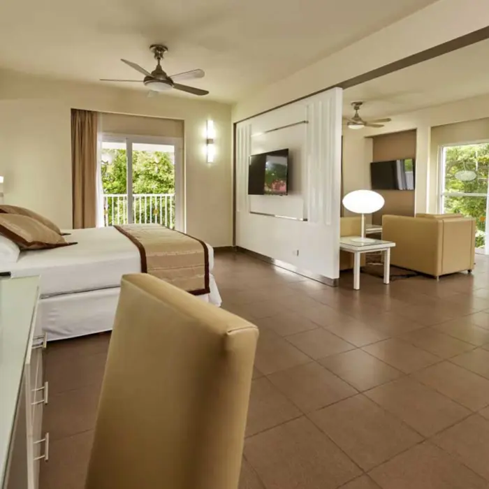 A spacious and elegantly furnished suite featuring a comfortable bed, a separate living area with a couch and TV, and a dining space.