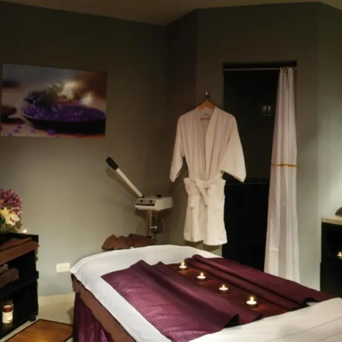 serene spa treatment room with a massage bed, a neatly folded white robe, a sink vanity, and candles for ambiance.