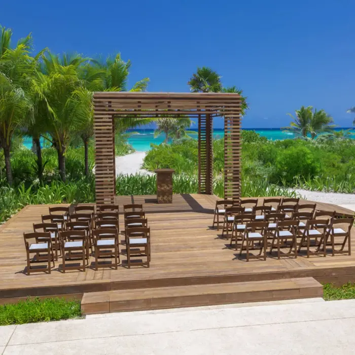 Garden gazebo wedding venue with wooden platform and dark chairs, surrounded by lush palms and a view of the ocean.