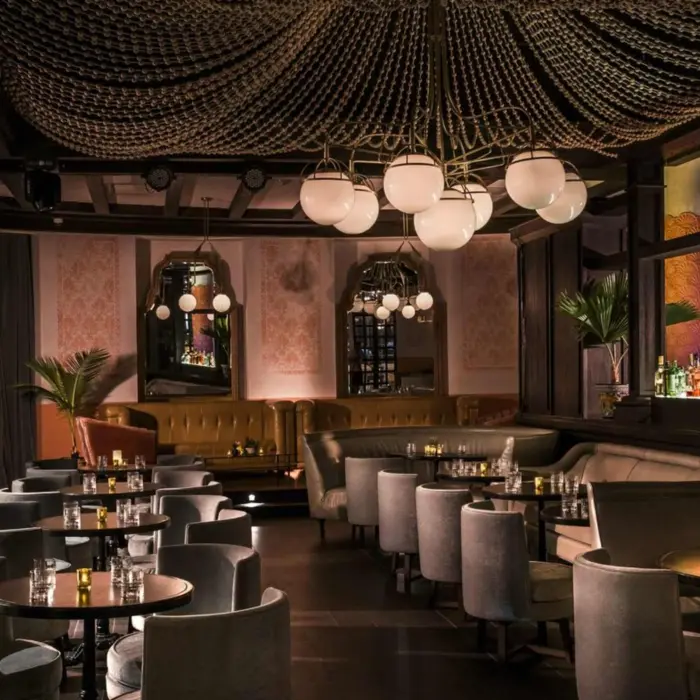 Upscale cocktail bar with plush seating, dramatic beaded ceiling fixture, and softly lit bottles behind the bar.