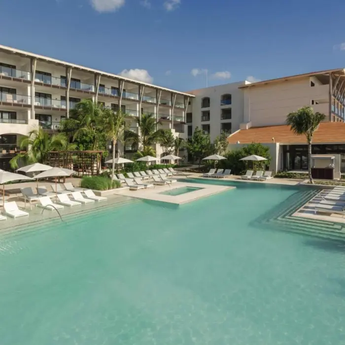 Loungers and umbrellas surround a modern infinity pool with in-water seating at a luxury beachfront resort.