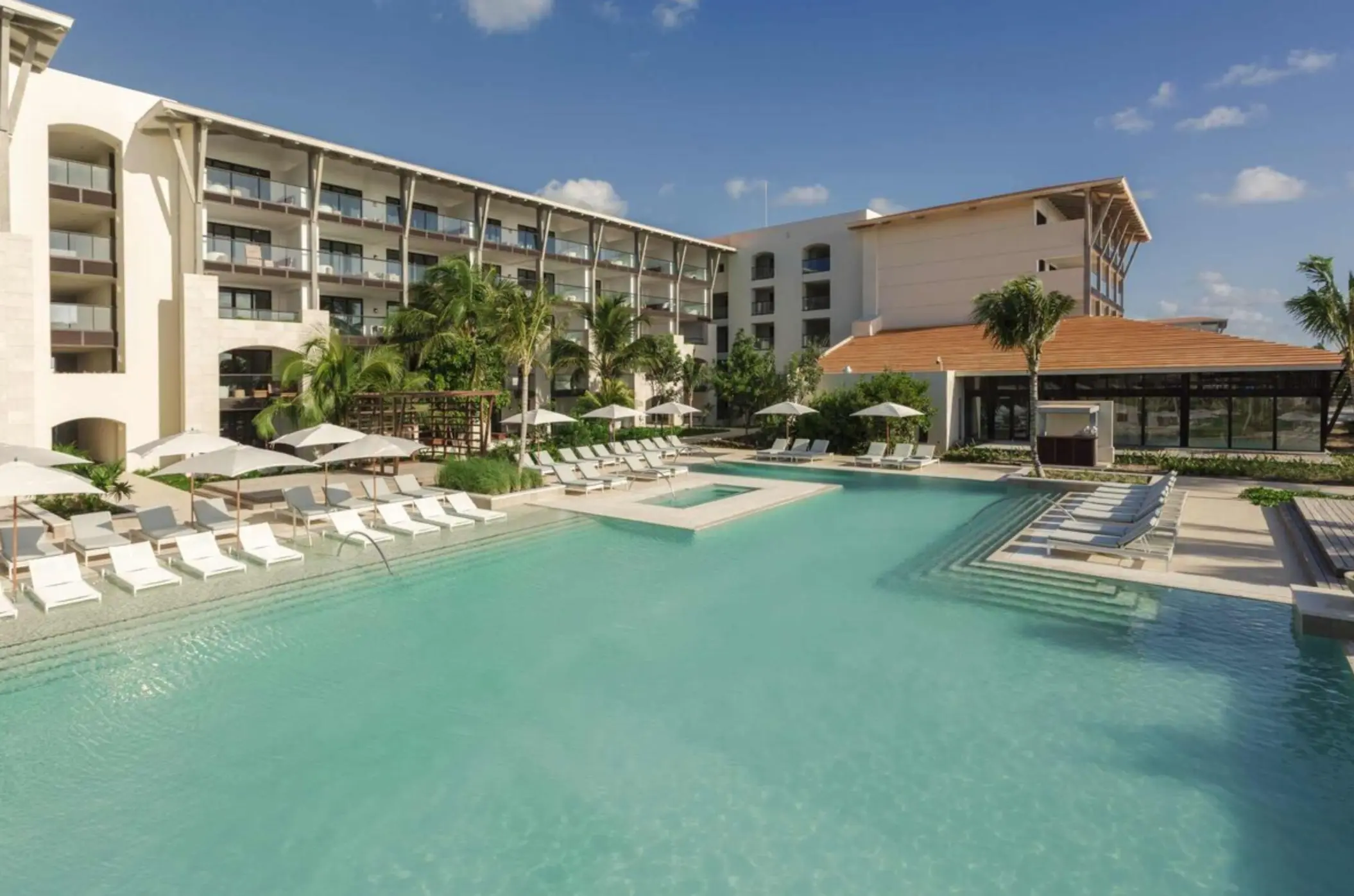 Loungers and umbrellas surround a modern infinity pool with in-water seating at a luxury beachfront resort.