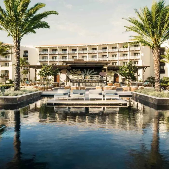 Resort pool surrounded by loungers, palm trees, and a large bar, with suites overlooking the courtyard.