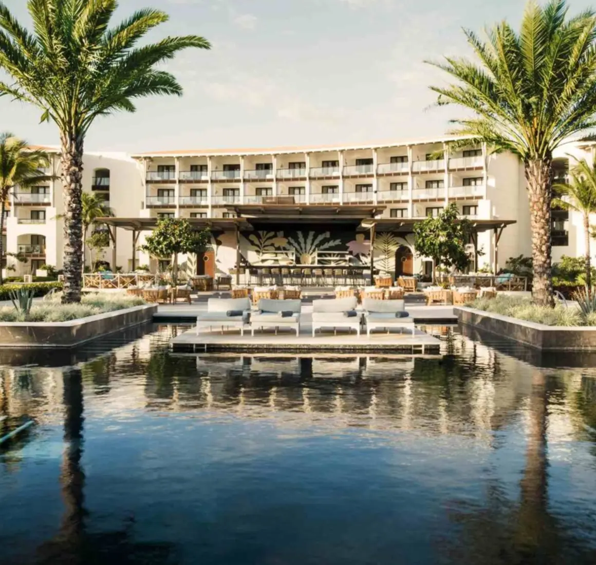 Resort pool surrounded by loungers, palm trees, and a large bar, with suites overlooking the courtyard.