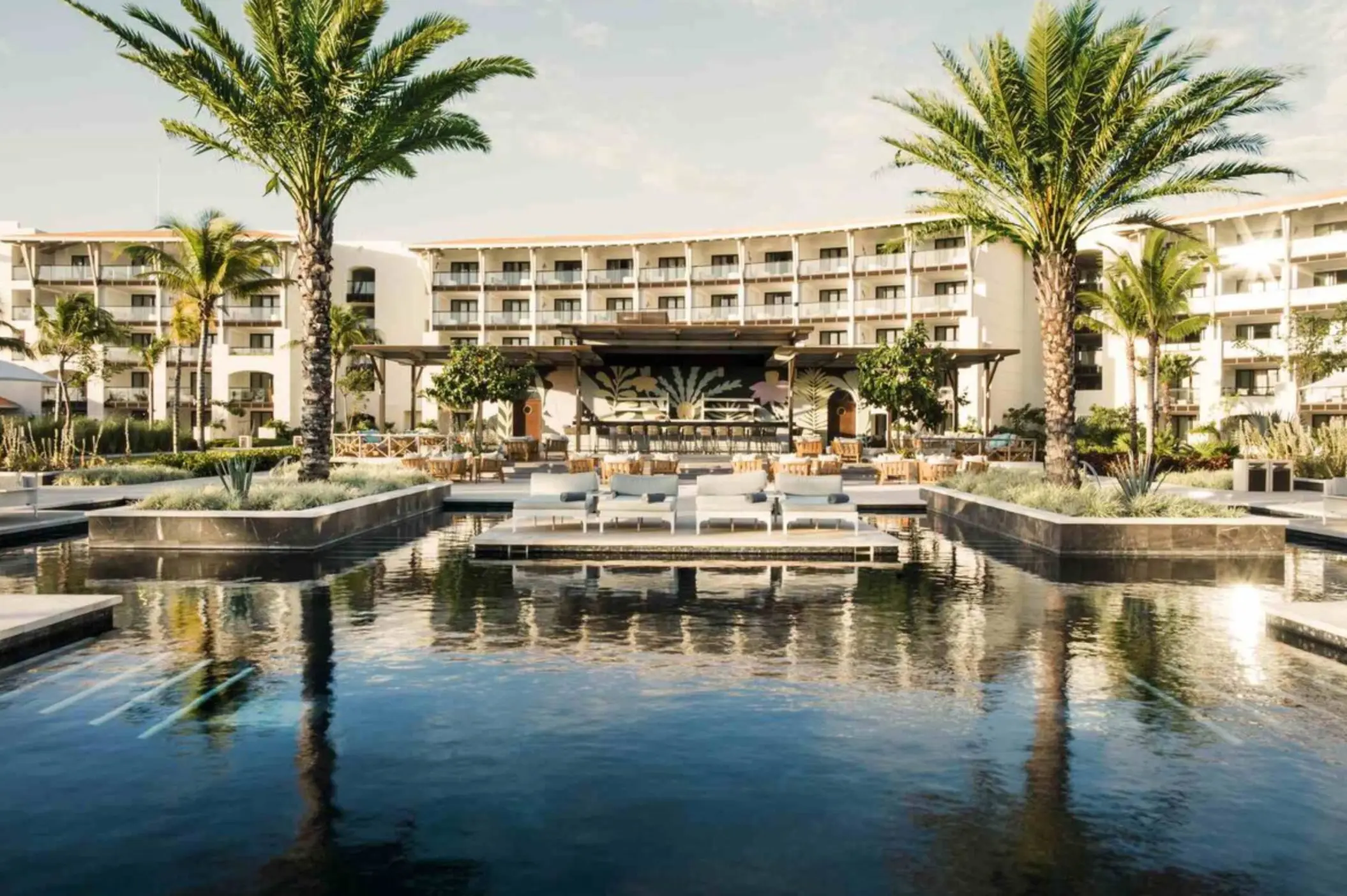 Resort pool surrounded by loungers, palm trees, and a large bar, with suites overlooking the courtyard.