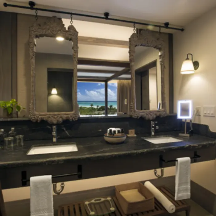 Elegant bathroom with dual sinks, framed mirrors, and window view overlooking ocean and palm trees.