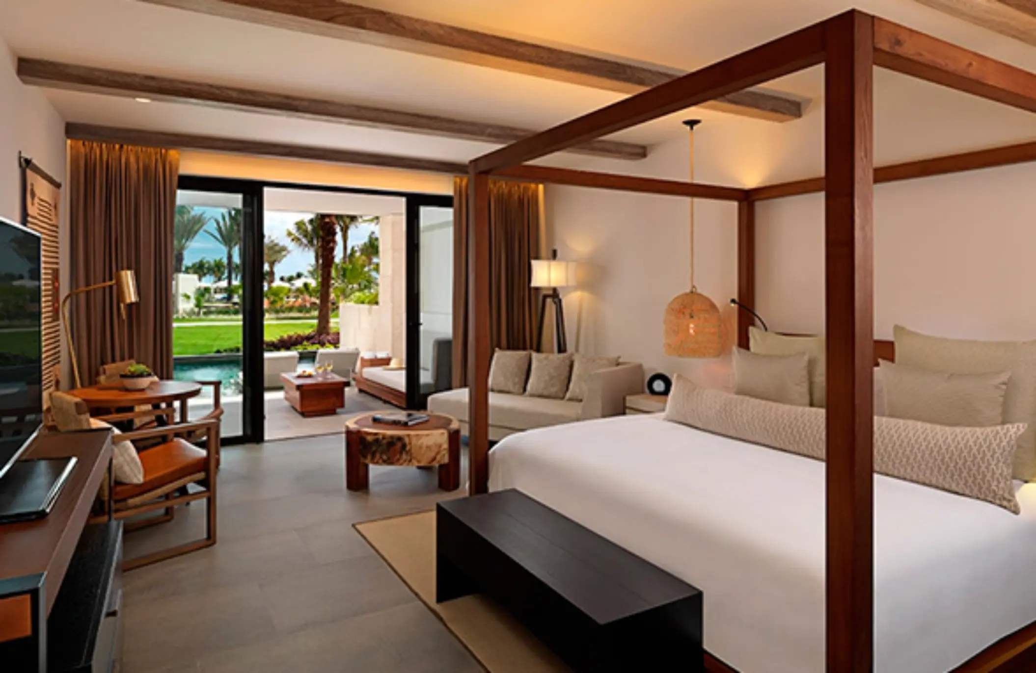 Luxury suite with garden and pool views, featuring a canopy bed, warm lighting, and terrace seating area.